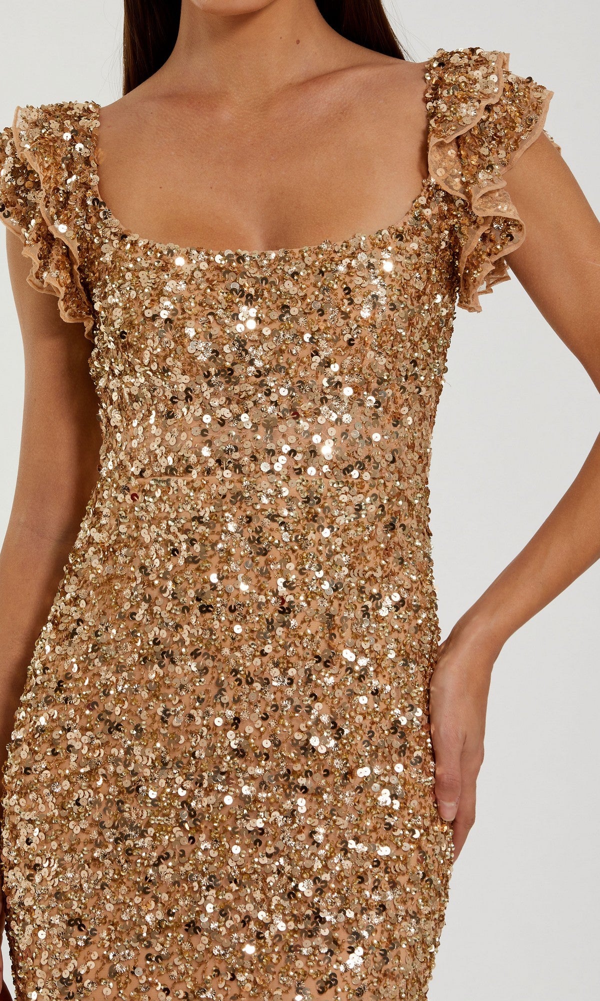 A woman wears the Mac Duggal 94279 long formal dress in gold sequins, featuring ruffled cap sleeves, with one hand on her hip, shown from shoulders to mid-thigh.